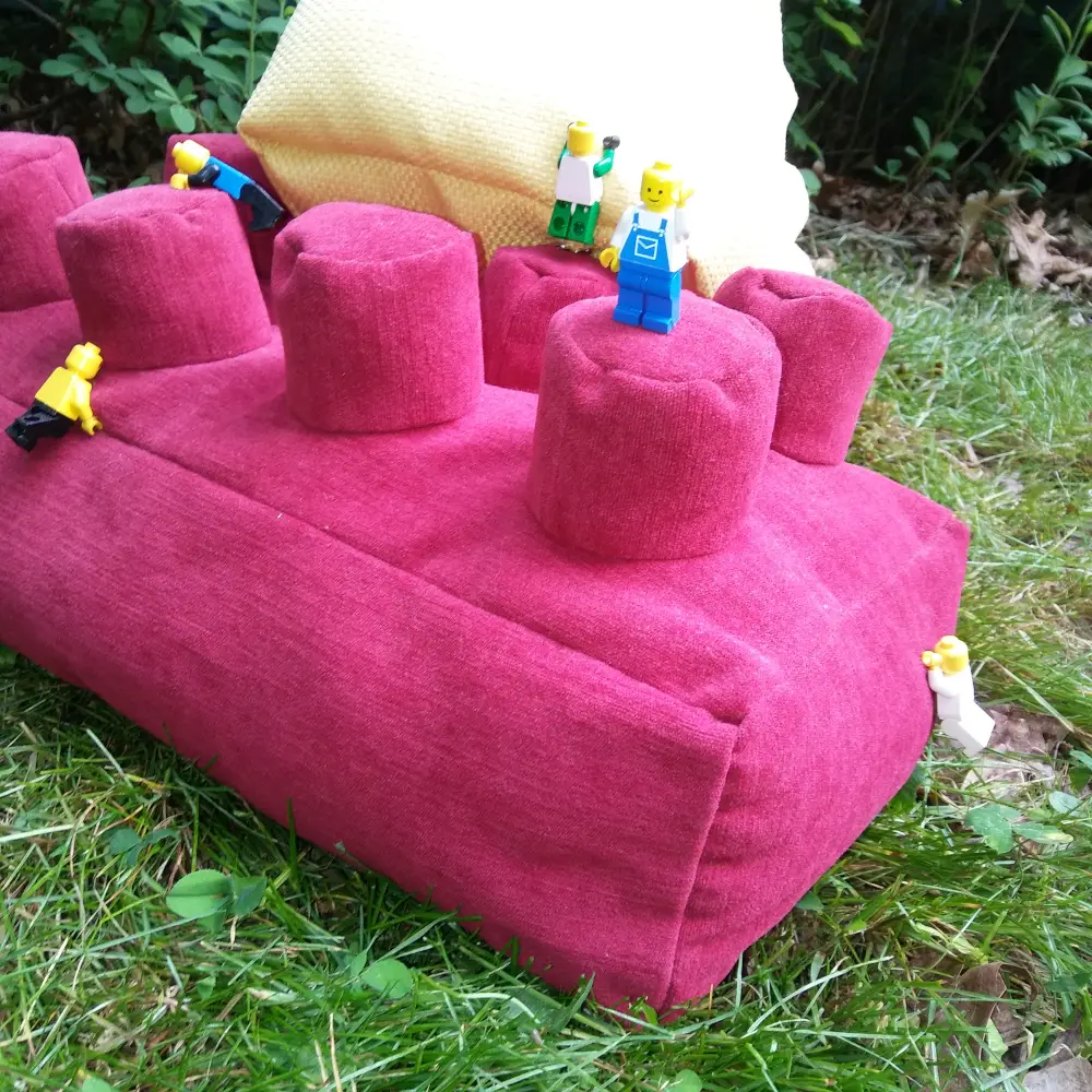 lego minifigures climbing on lego brick-shaped throw pillow