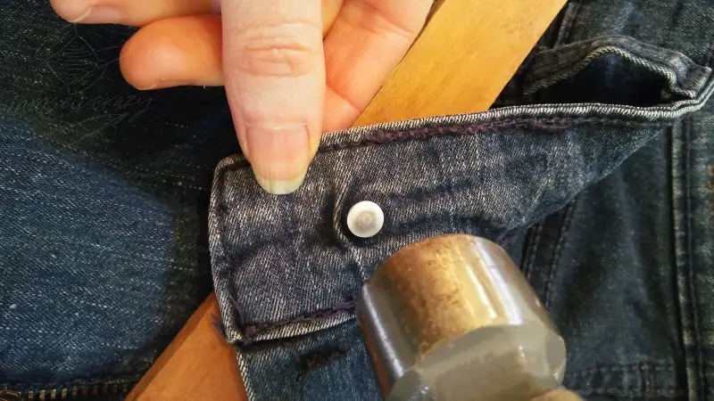 hammering new button onto jeans