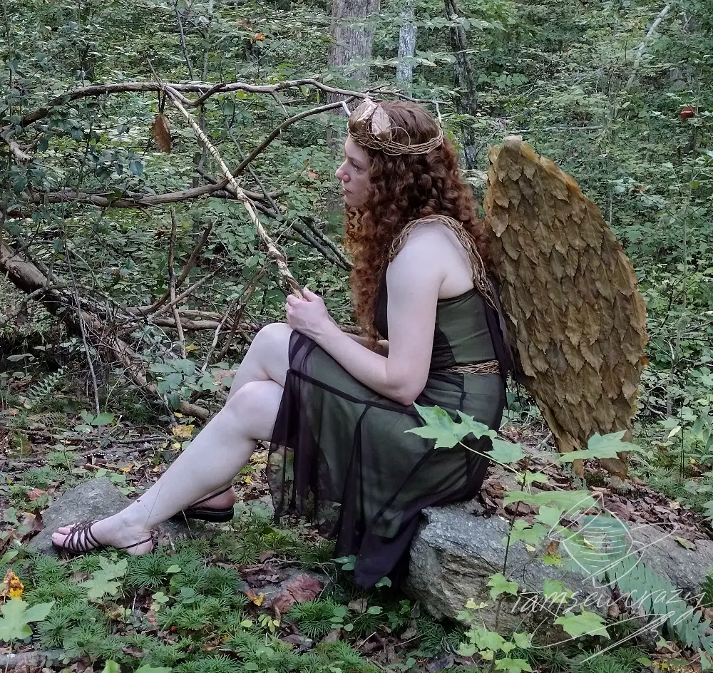redhaired woman dressed as woodland fairy sitting on rock