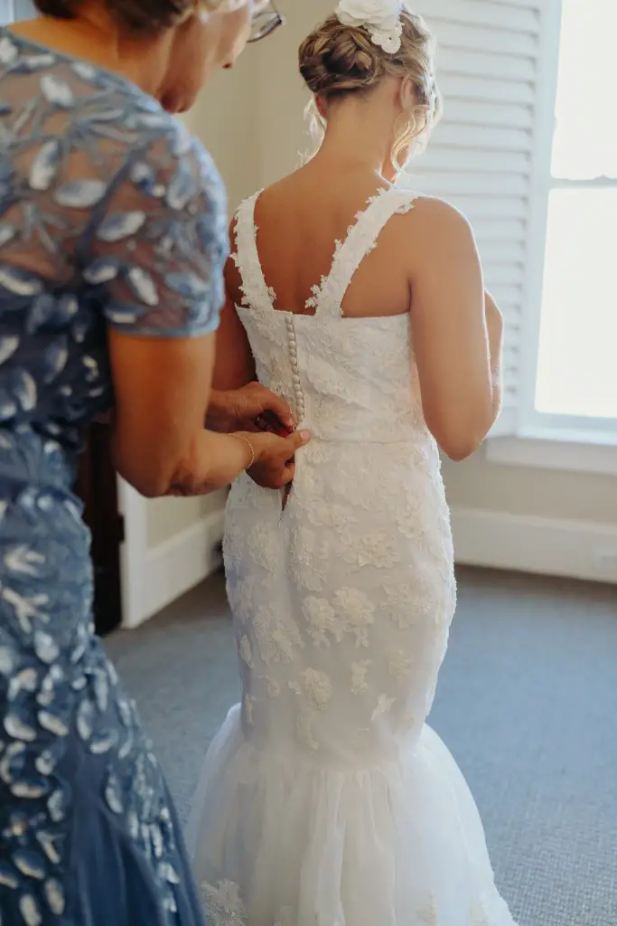 woman helping her daughter put on wedding dress