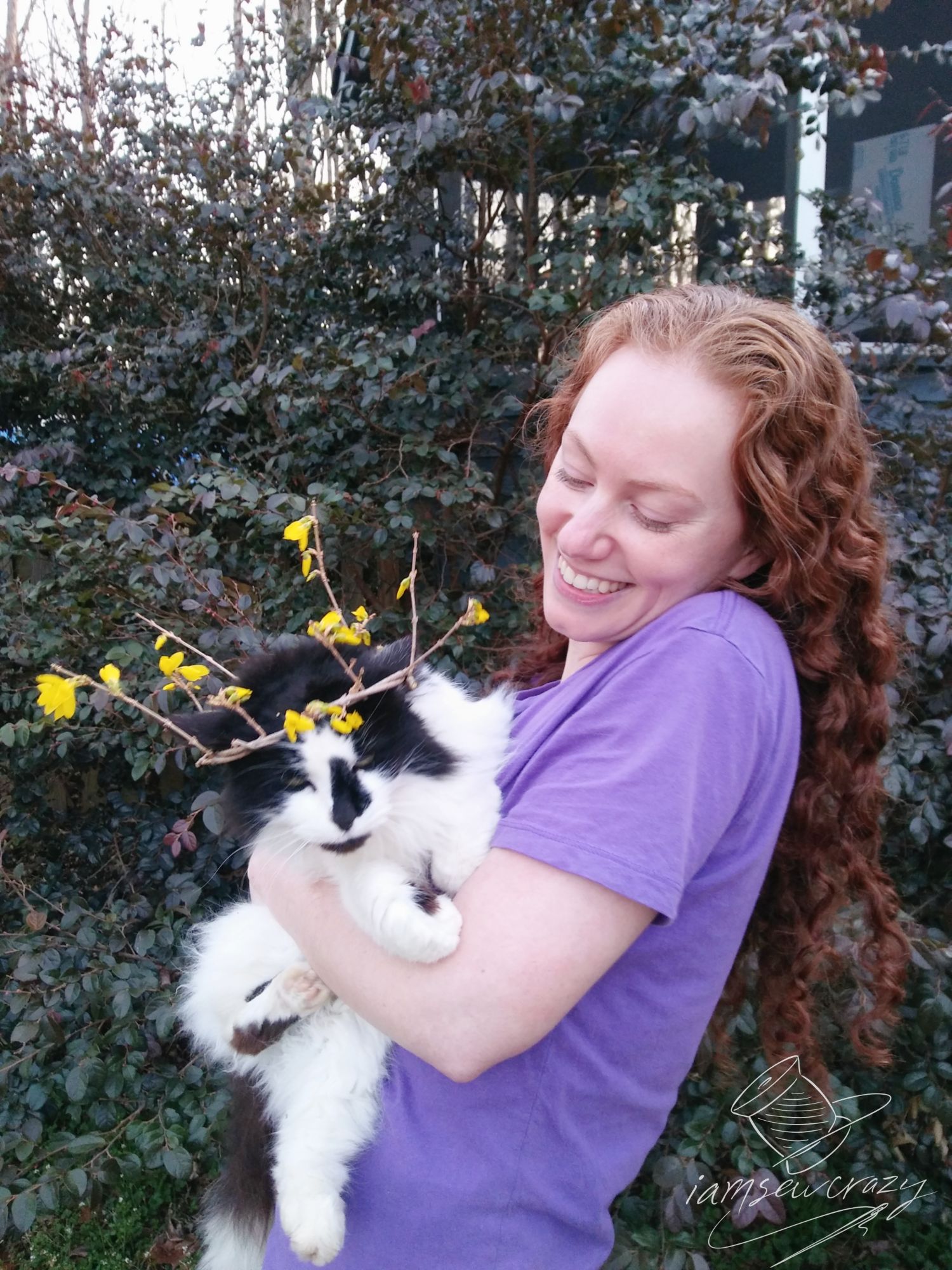 red-haired woman holding black and white cat wearing a crown made of flowers